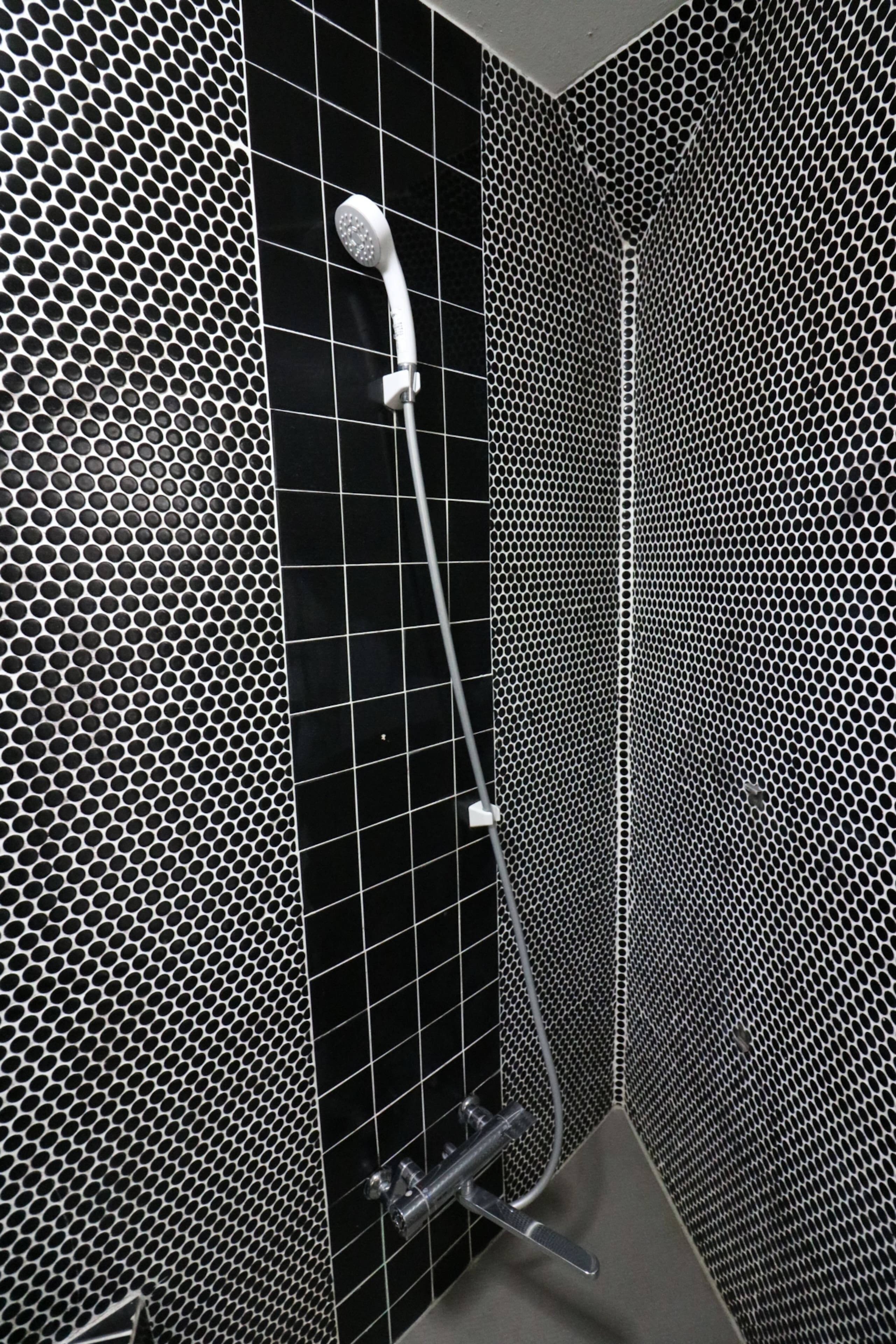 A modern bathroom with a black and white hexagonal tile pattern, a shower with a handheld showerhead, and a visible drain.