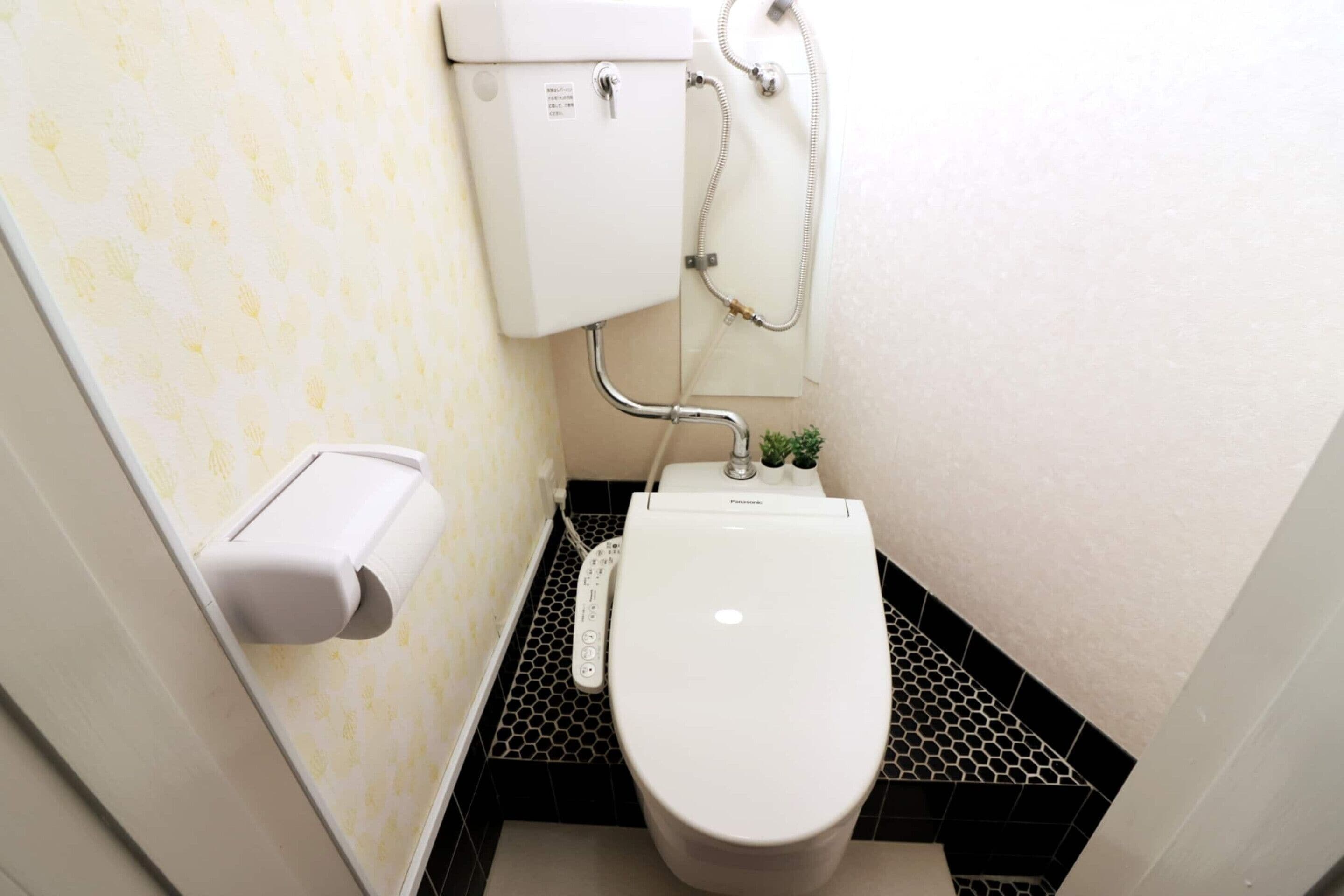 A small bathroom with a toilet, a toilet paper holder, and a shower control panel.