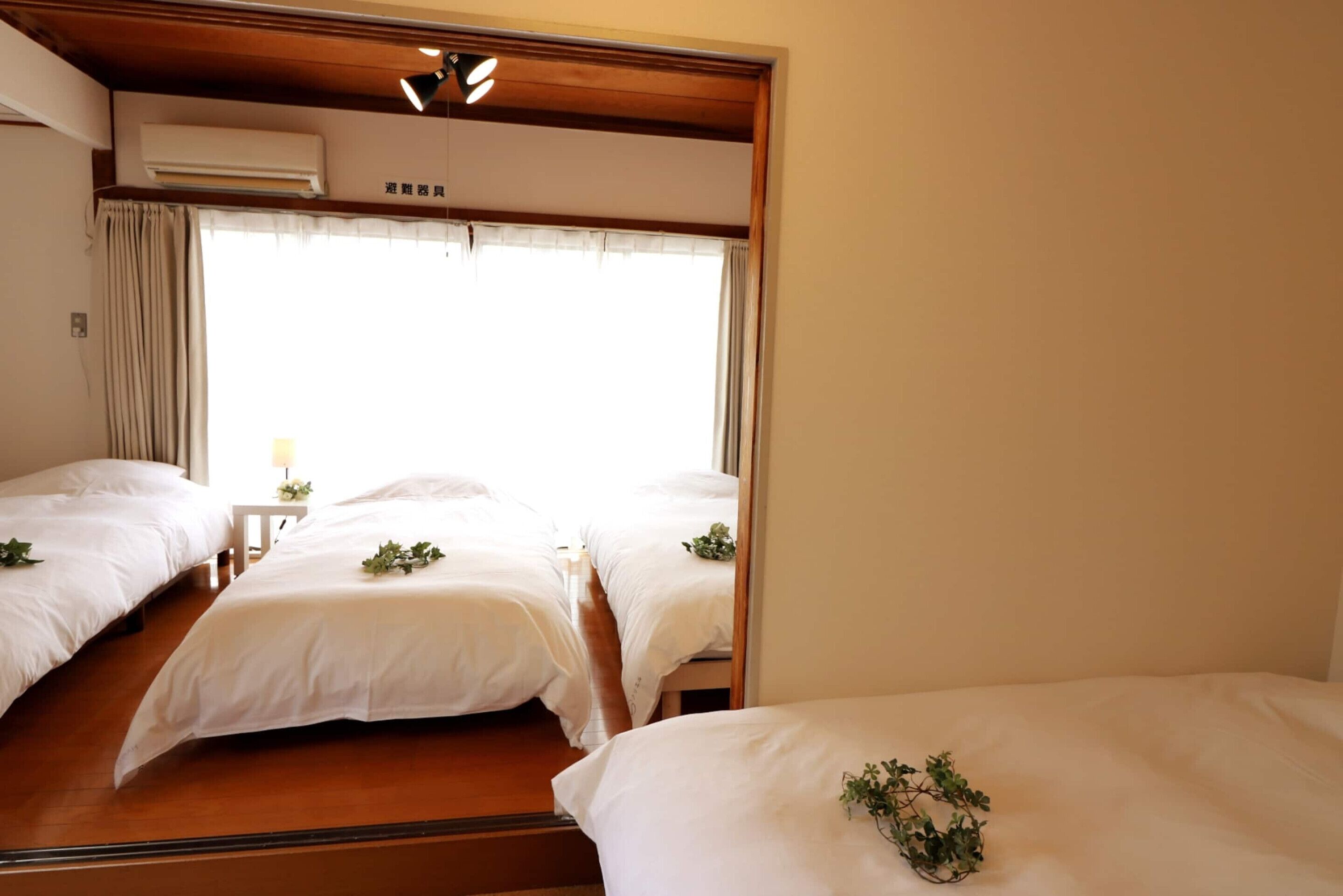 A hotel room with two beds, a wooden ceiling, an air conditioning unit, and a window with curtains.