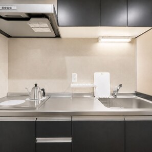 A modern kitchen with a stainless steel countertop, a kettle, a sink, and a built-in range hood. - Hotel Piacere Namba (Osaka)