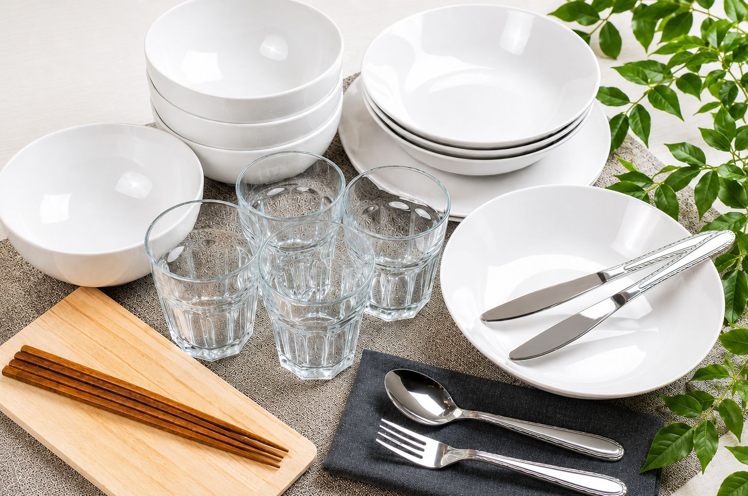 A set of white dinnerware including bowls, plates, and glasses, along with cutlery and a wooden cutting board.
