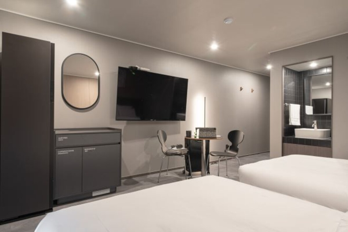 A modern hotel room with a large bed, a desk with a chair, a television, a mirror, and a wardrobe.