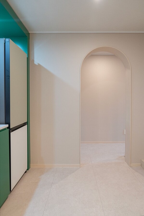 Un couloir avec une armoire verte et blanche, un sol carrelé et un mur sobre avec une porte au fond.