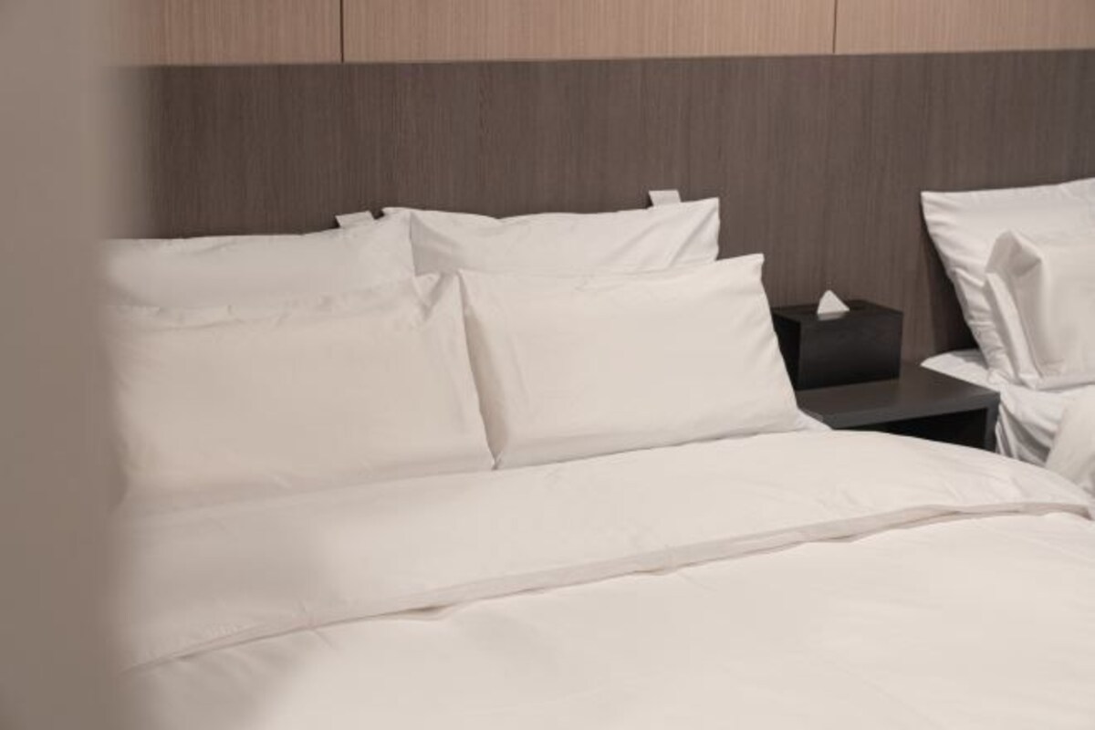 A neatly made bed with white linens and pillows, a bedside table with a tissue box, and a wooden headboard.