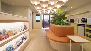 A modern reception area with a checkered ceiling, a seating area with a plant, and a counter with a coffee machine. - Workers Hotel Ansan by Anook (Ansan)