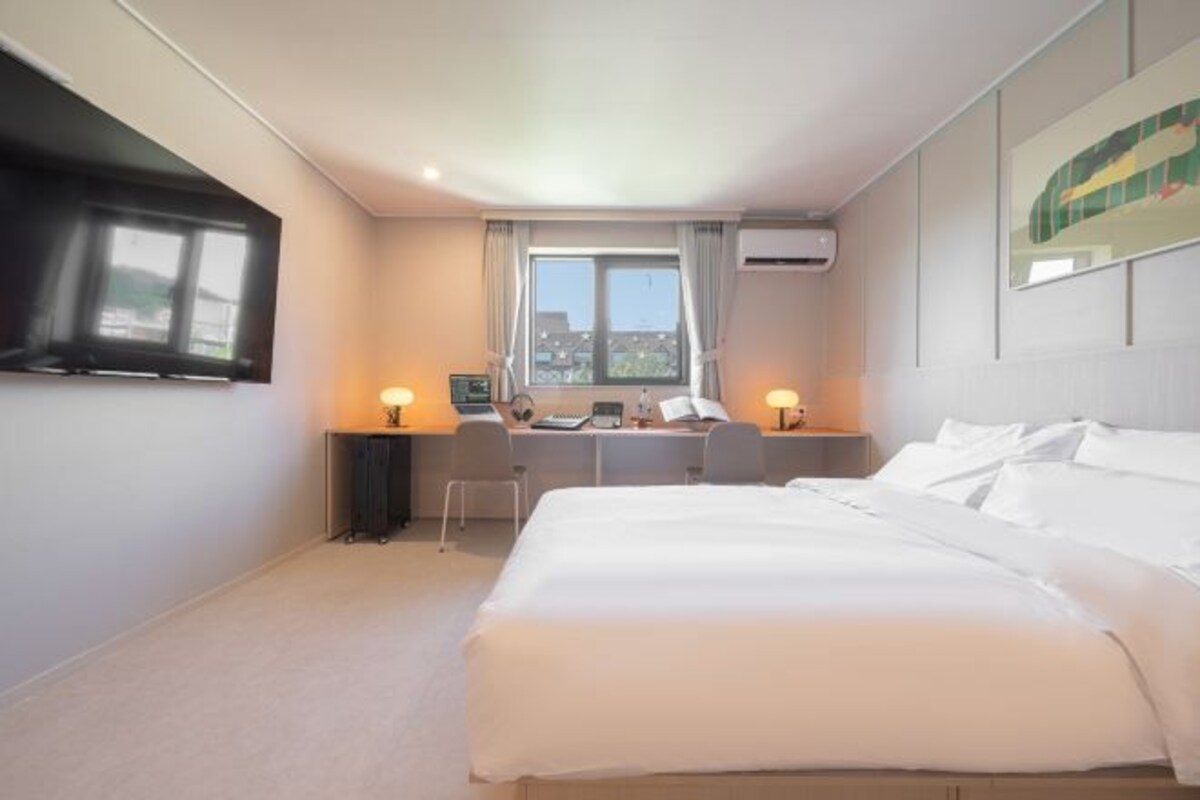 A hotel room with a large bed, a desk with two chairs, a window with curtains, and an air conditioning unit.