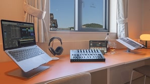 A workspace with a laptop, headphones, a mixer, and a glass of whiskey on a desk by a window with curtains. - Workers Hotel Ansan by Anook (Ansan)