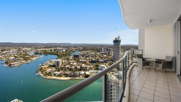 Un balcón con vista a una ciudad costera, incluyendo un edificio alto y una masa de agua.