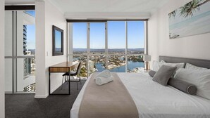 Habitación de hotel con una cama grande, un escritorio y vistas a un paisaje urbano y al agua.