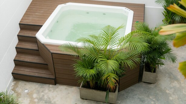 Un bain à remous avec des marches en bois menant à l’intérieur, entouré de plantes en pot.