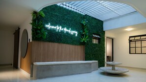 Un espace d’accueil agrémenté d’un mur végétal, d’un panneau lumineux néon, d’un panneau en bois, d’un banc en béton et d’une fontaine ronde.
