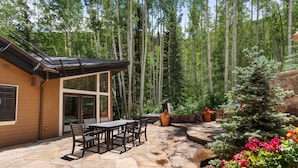 Eine Terrasse mit Steinböden, einem Holztisch mit Stühlen, einem Grill und einem Blumentopf.