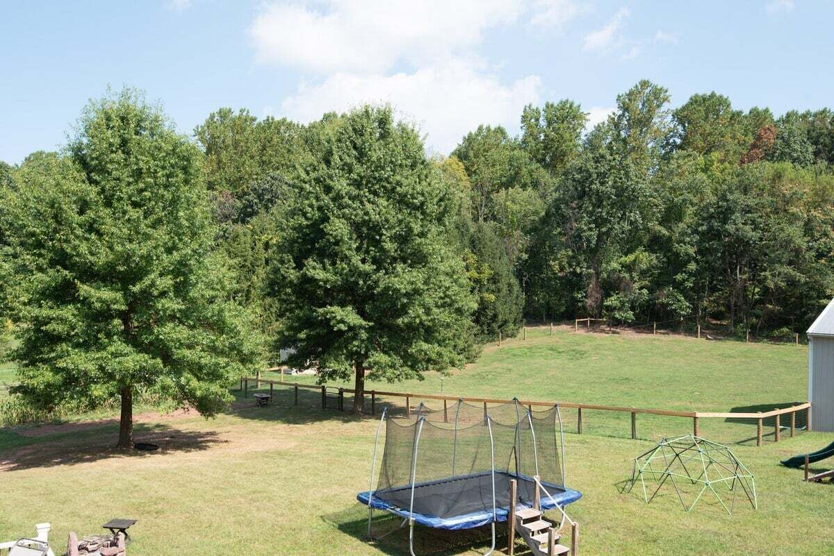 Un patio trasero con un trampolín, un columpio de madera y una zona de juegos cercada.