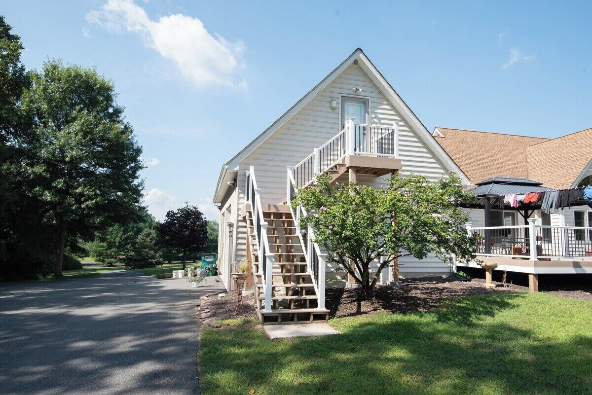A two-story house with a front porch, a staircase leading to the second floor, and a small tree in the front yard.