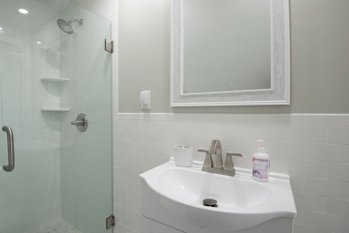 A bathroom with a glass-enclosed shower, a white sink with a mirror above it, and a hand soap dispenser.
