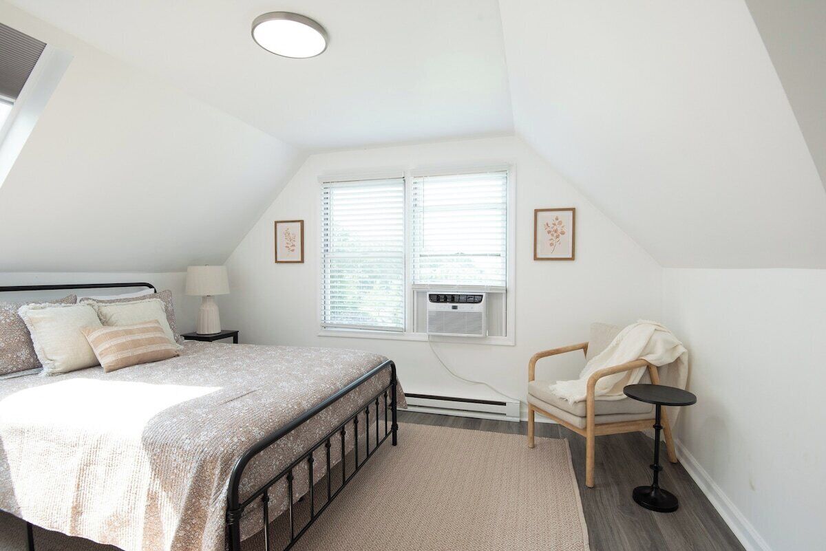 Un dormitorio con cama, mesita de noche, silla y ventana con persianas.