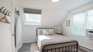 Ein Schlafzimmer mit Bett, Fenster, Tür und Kleiderhaken.