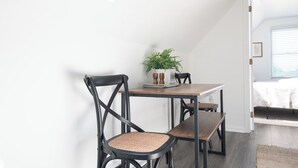 Ein Essbereich mit Tisch und Stühlen, einer Pflanze auf dem Tisch und Blick ins Freie durch ein Fenster.