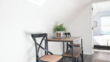 Uma área de refeições com mesa e cadeiras, uma planta sobre a mesa, e vista para o exterior através de uma janela.