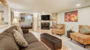 A cozy living room with a sofa set, a fireplace, a television, and a vibrant floral artwork on the wall.