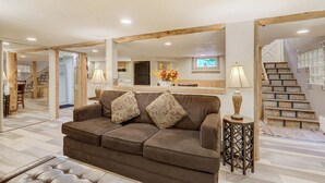 A living room with a brown sofa, patterned cushions, a side table with a lamp, and a mirror above the sofa.