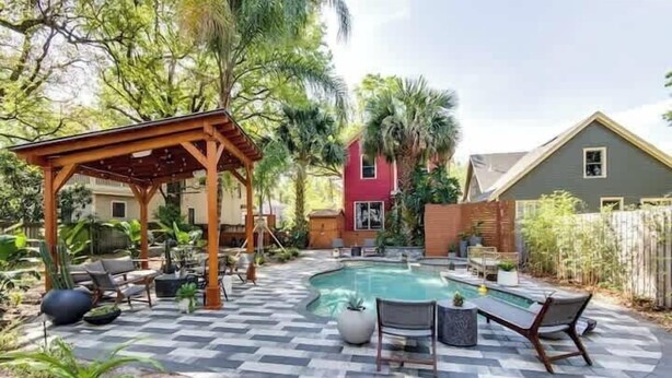 Um quintal com piscina, móveis de pátio e uma pérgola de madeira.