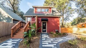 Uma casa vermelha com varanda da frente, escada e um caminho sinuoso que leva à porta.