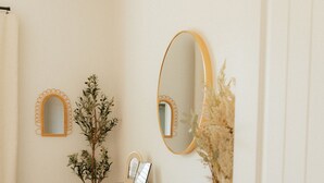 Una habitación con un aparador oscuro, dos espejos en la pared, una planta pequeña y una puerta.