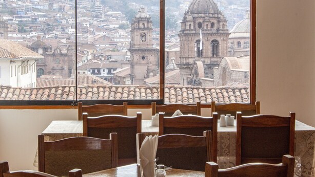 Un comedor con una mesa lista para dos, con vistas a un paisaje urbano que incluye edificios históricos y una iglesia destacada.