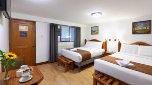 Habitación de hotel con dos camas, un escritorio de madera con un jarrón de girasoles y un cuadro en la pared.