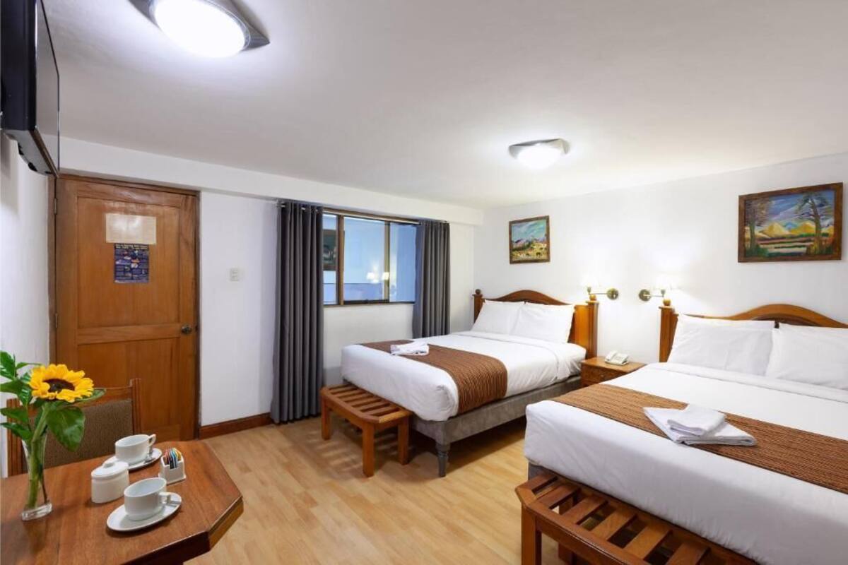 A hotel room with two beds, a wooden desk with a vase of sunflowers, and a painting on the wall.