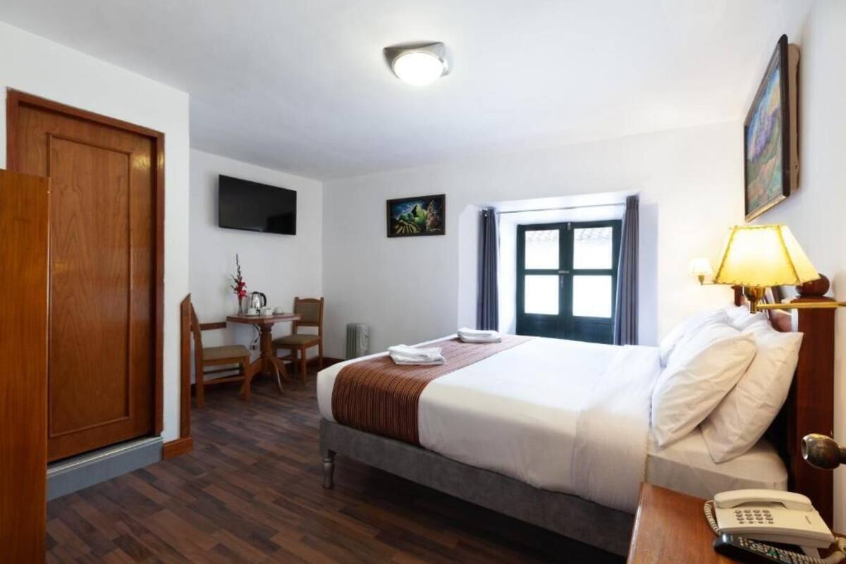 A hotel room with a bed, bedside table, lamp, and a desk with a chair.