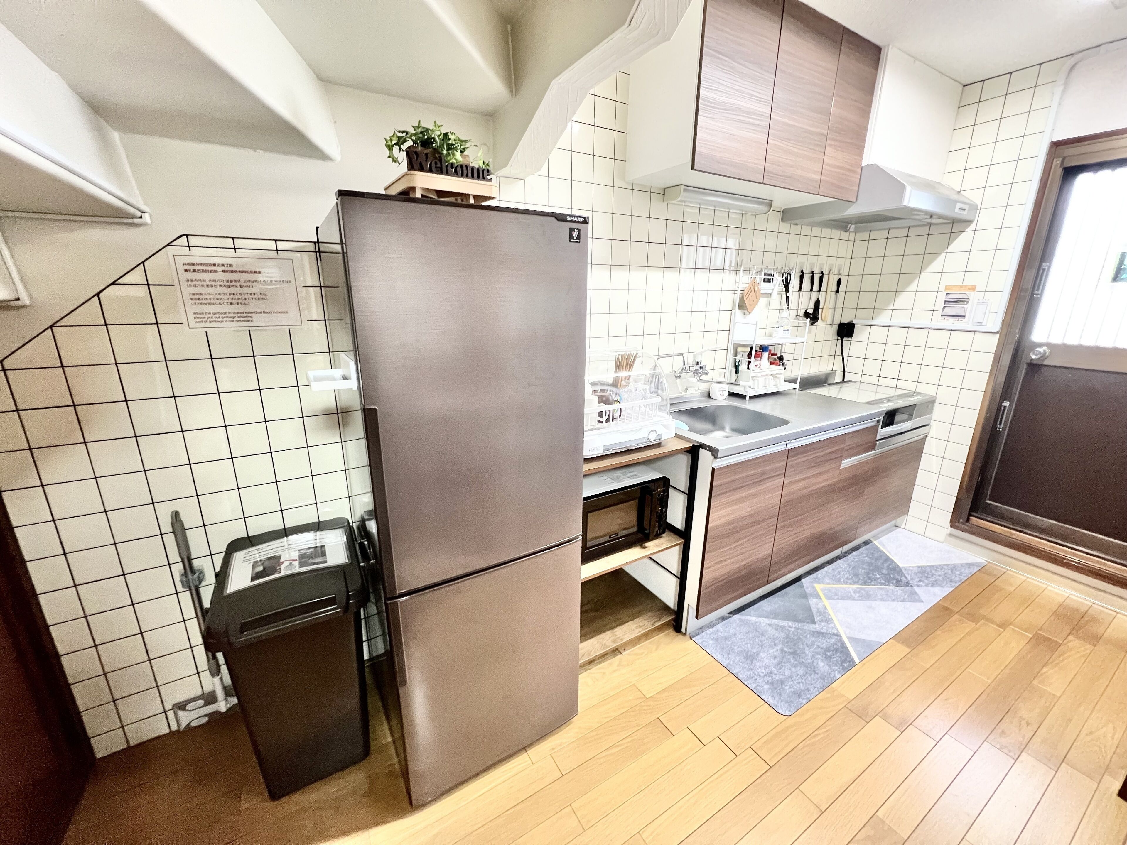 A compact kitchen with a stainless steel refrigerator, wooden cabinets, a tiled backsplash, and a built-in microwave.