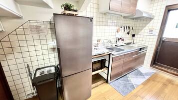 A compact kitchen with a stainless steel refrigerator, wooden cabinets, a tiled backsplash, and a built-in microwave.