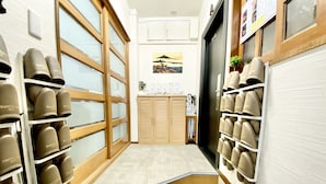 A narrow hallway with shoe displays on both sides, a welcome mat at the entrance, and a door with a view of a landscape. - GuestHouse Reina osaka (Osaka)
