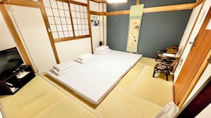 A traditional Japanese-style room with tatami flooring, a futon bed, a television, and a shoji screen. - GuestHouse Reina osaka (Osaka)