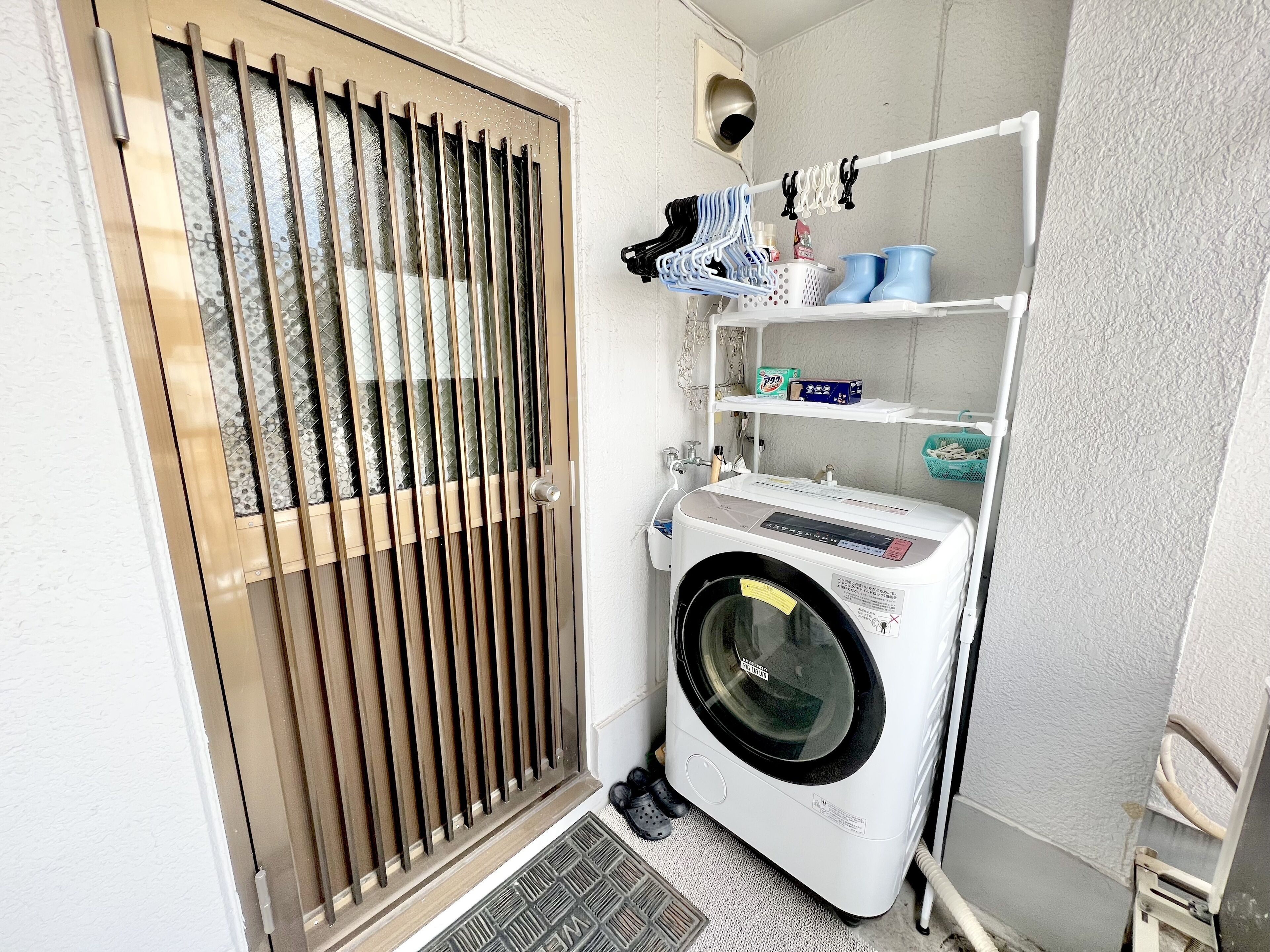 A laundry room with a front-loading washing machine, a drying rack, and shelves with laundry supplies.