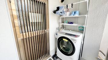A laundry room with a front-loading washing machine, a drying rack, and shelves with laundry supplies.