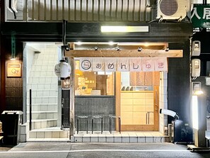 Un restaurante con decoración de madera, un cartel y tres taburetes en el exterior.
