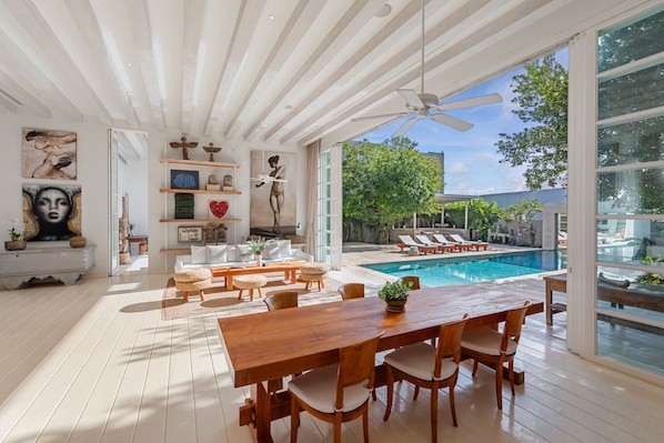 Relax in a spacious living area with a large dining table and comfortable seating, overlooking a pool.