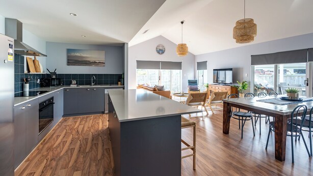 A modern kitchen with a central island, dark cabinetry, and a dining area with a large table and chairs. - Spacious 4x3 home, just minutes away from the Margaret River main street. (Margaret River)
