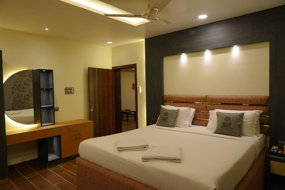 A hotel room with a large bed, a wooden headboard, a nightstand, a mirror, and a vanity with a sink.