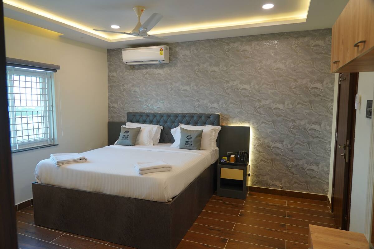 A modern hotel room with a large bed, a nightstand, a ceiling fan, and a textured wall.