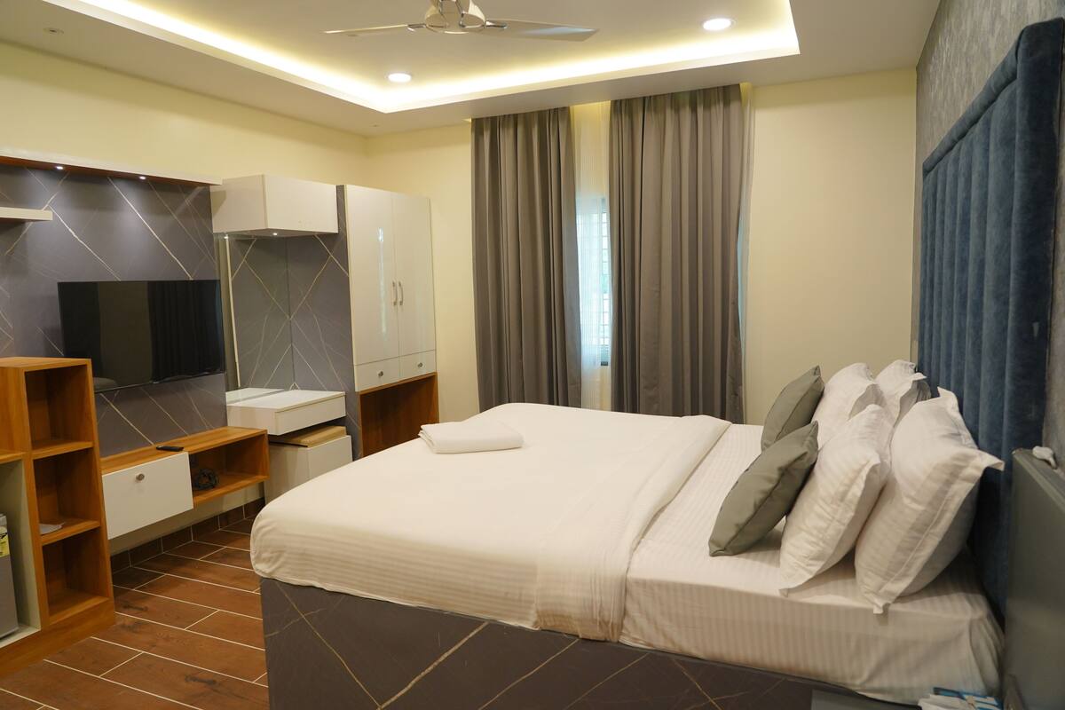 A modern hotel room with a large bed, a TV, a wardrobe, and a bathroom.