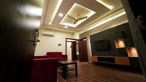 A modern living room with a ceiling fan, red sofas, a TV, and a wooden entertainment unit. - Mevid hotels (Hyderabad)