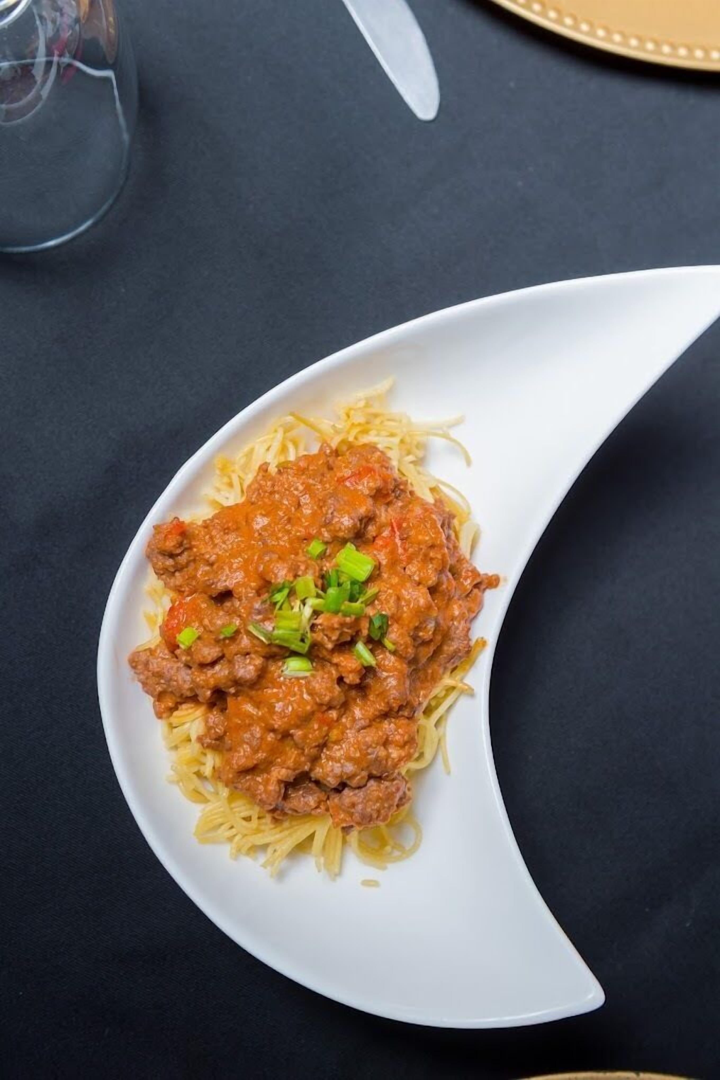 Um prato de espaguete com molho de carne e decoração sobre uma mesa escura.