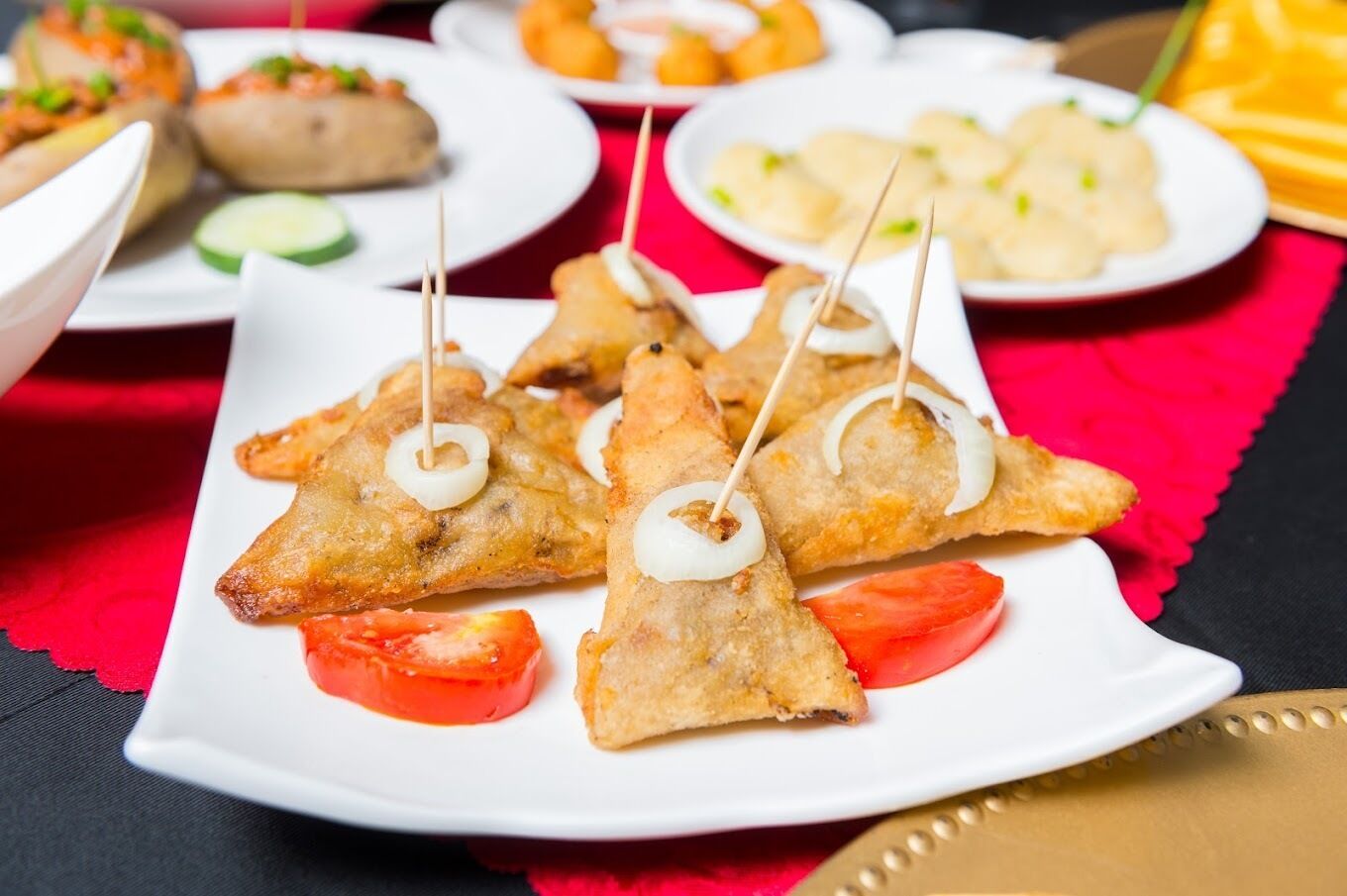A plate of triangular-shaped fried food items with toothpicks, accompanied by slices of tomato and cucumber.