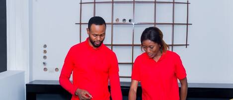 Dos personas con camisetas rojas de pie en la recepción de un interior moderno con un muro de diseño tipo cuadrícula y un mostrador de madera.