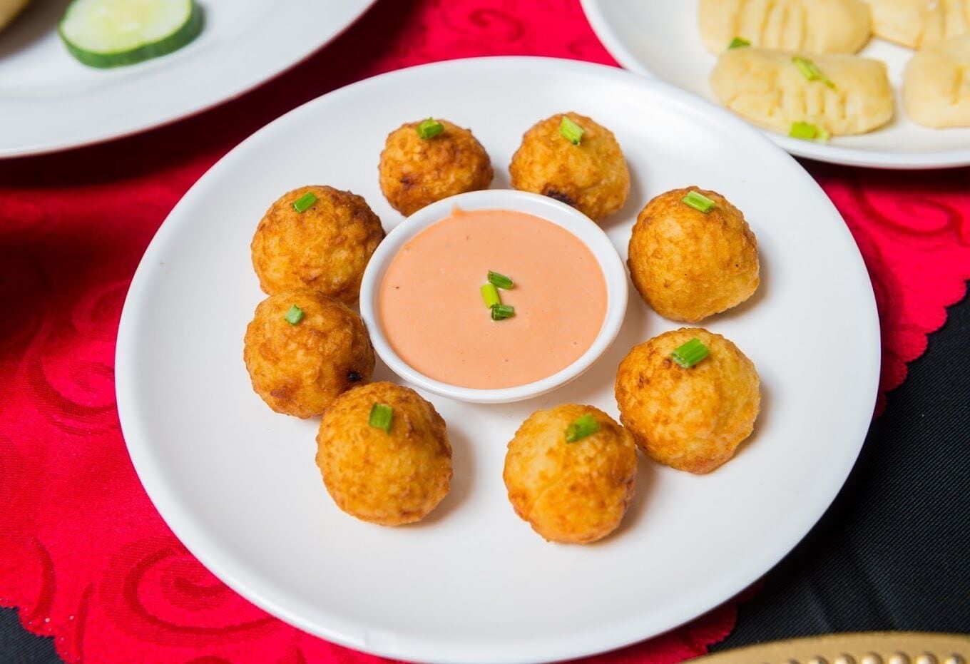 A plate of fried balls with a dipping sauce and a plate of dumplings in the background.
