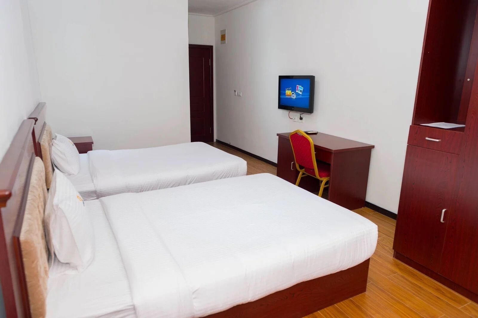 Hotellihuone, jossa on kaksi erillistä sänkyä, työpöytä tuolilla, televisio ja vaatekaappi.